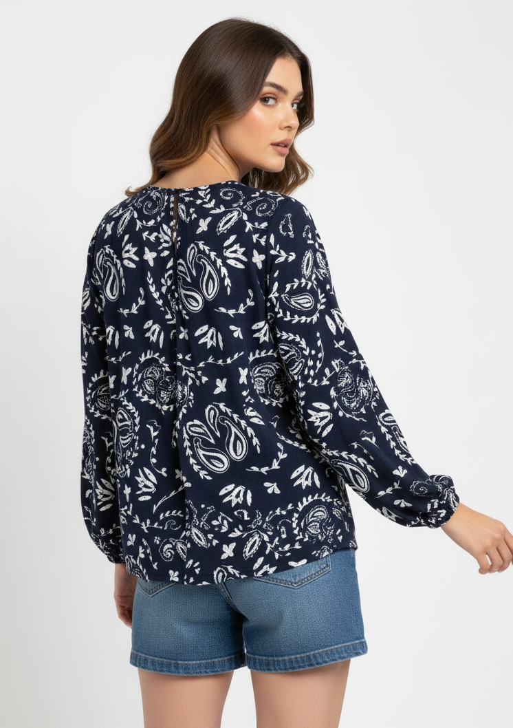 Woman wearing a navy blue patterned blouse and denim shorts on a white background
