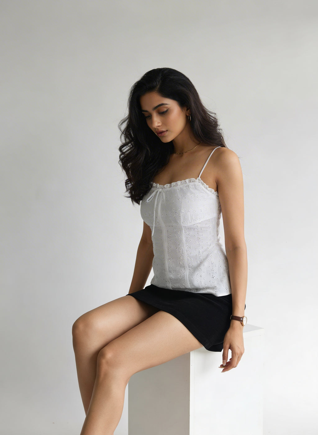 Woman wearing a white top and black shorts sitting on a white surface with a plain background