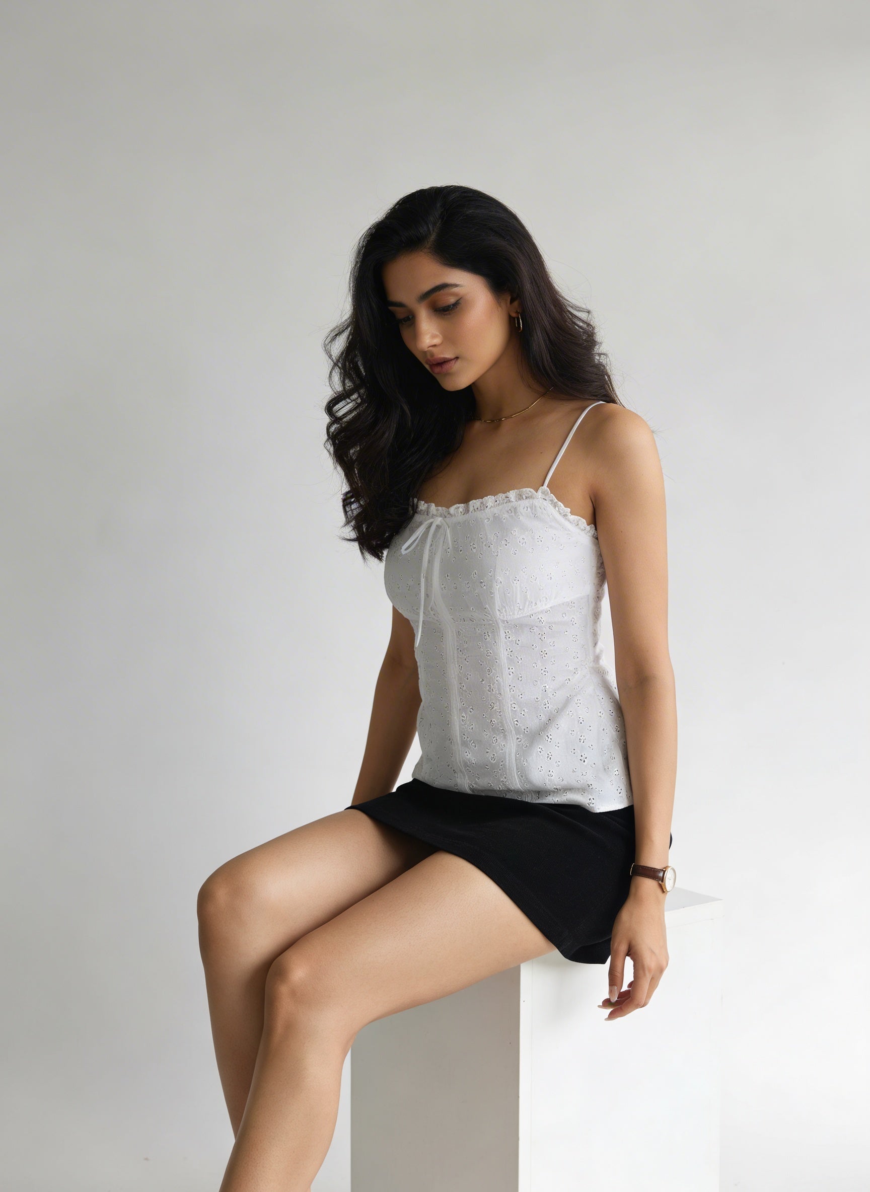 Woman wearing a white top and black shorts sitting on a white surface with a plain background