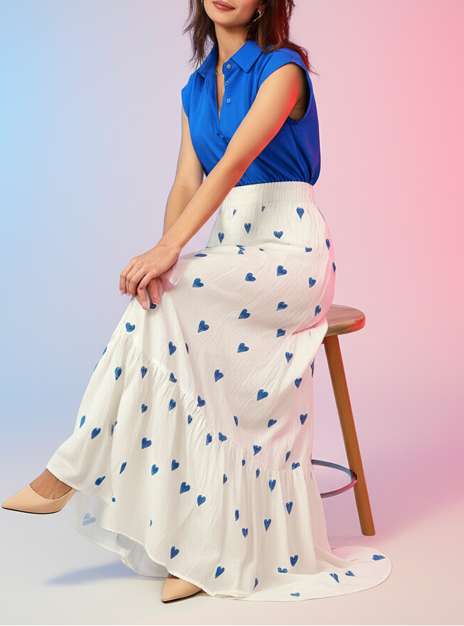 Woman sitting on a stool wearing a blue top and white skirt with blue heart patterns against a gradient background.